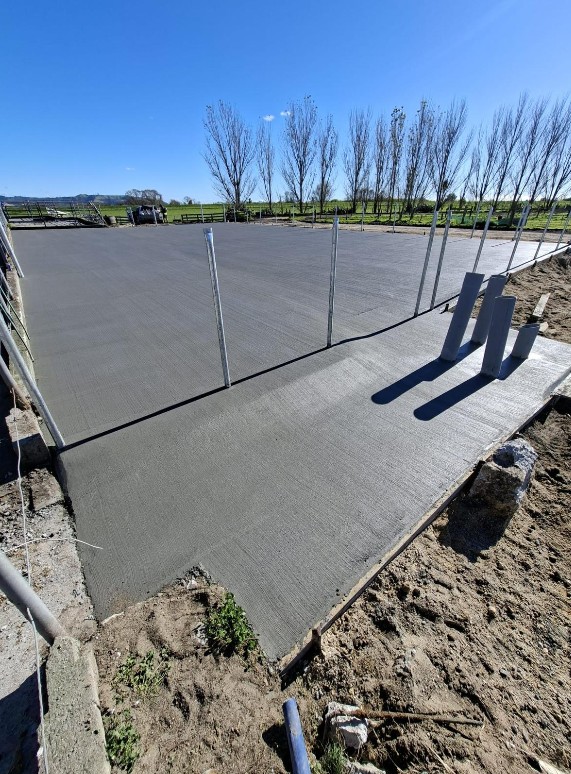 Freshly poured concrete farm pad framed by post and rail fencing in Tauranga